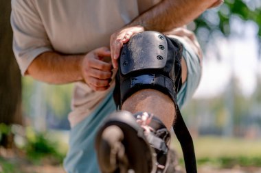 Paten kaymaktan yorulan genç bir adamın dizine yakın plan. Parkta diz çökmüş ve büyük beden bir model.