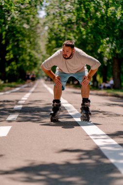 Sakallı genç adam şehir parkında paten kaymayı öğreniyor. Yeni şeyler öğrenmek ve vücut pozitifliği.