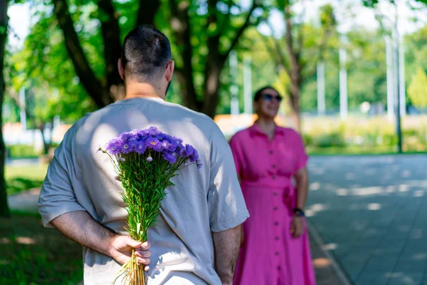 若いカップル男は公園で女の子に会い 彼の背後にある花束とサイズモデルを隠します — ストック写真