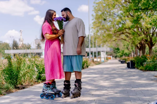 ローラースケートの若いカップル男は 公園で日付中に花束を女の子に与える — ストック写真
