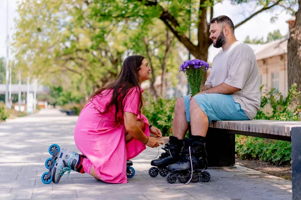 Young Couple Girl Helps Guy Put Rollerblades Who Sitting Park — Stock Photo, Image