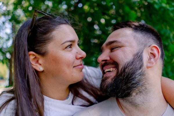 公園の背景とサイズモデルのデート中に抱擁とキスに立っている男と女性の若いカップルの肖像画 — ストック写真