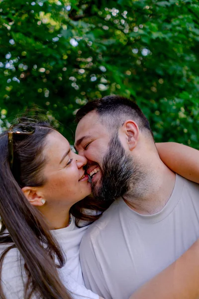 公園の背景とサイズモデルのデート中に抱擁とキスに立っている男と女性の若いカップルの肖像画 — ストック写真