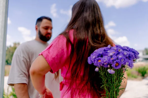 Young couple girl hides a bouquet of flowers from her boyfriend behind her back during date in the park