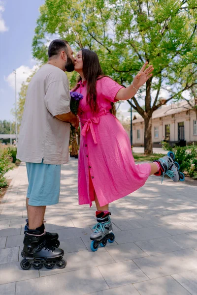 若いカップル男は公園でローラースケートデート中に花の少女の花束を与え 彼女にキス — ストック写真