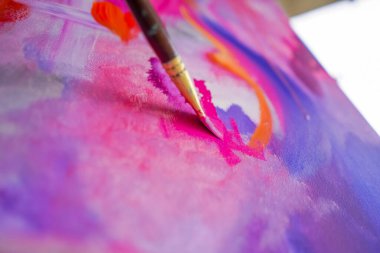 Bir resim stüdyosunun sehpasında duran bir ressama yağlı boya uygulayan bir fırçayla yakın plan bir resim.