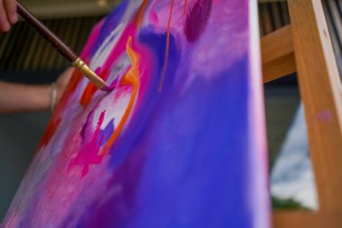 Bir resim stüdyosunun sehpasında duran bir ressama yağlı boya uygulayan bir fırçayla yakın plan bir resim.