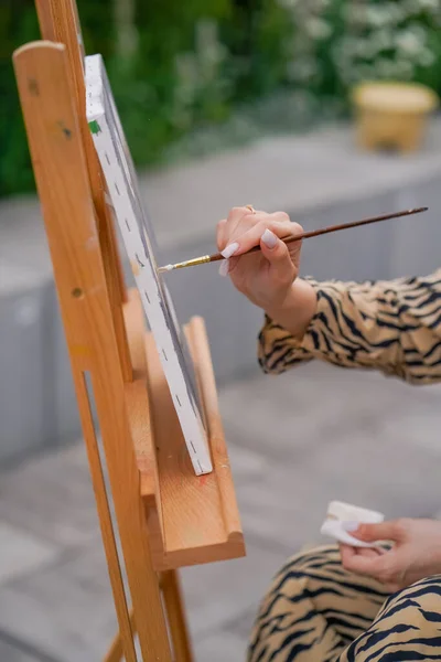 Close-up of a girl artist brushes oil paint on a painting standing on an easel in studio for painting on the street