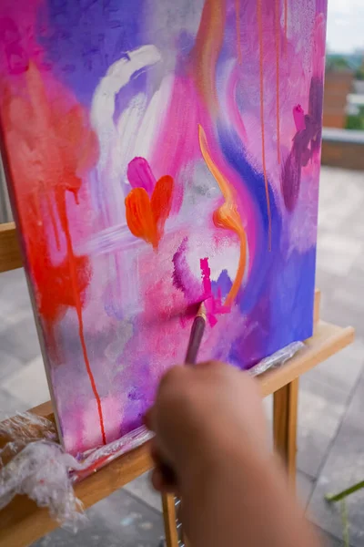 Close-up of a girl artist with a brush applying oil paint to a painting standing on easel in a studio for painting