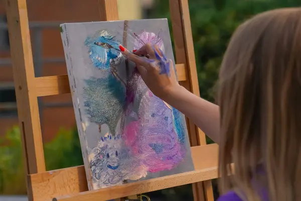 Close-up of a girl artist applying oil paint with a spatula to a painting in the process of creating painting