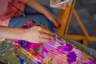 Resim sehpasının yanında oturan ve fırçalı bir paletin boyasını alan sanatçı bir kız. Güzel sanatlar aşkı kavramı.