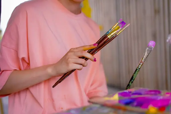 Close-up of girl artist taking paint brushes from a table during an art lesson concept of art appreciation