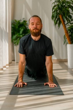 Sakallı yetişkin bir adam esneme ve sırt sağlığıyla aktif spor yaşam tarzında yerde yatıyor.