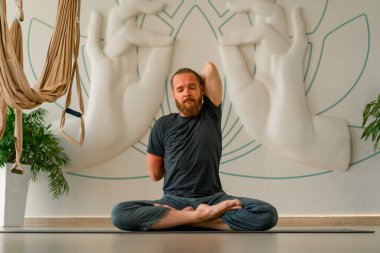 Sakallı yetişkin bir adam, parlak bir yoga stüdyosunda gözleri kapalı meditasyon yapar.