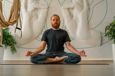 Sakallı yetişkin bir adam, parlak bir yoga stüdyosunda gözleri kapalı meditasyon yapar.