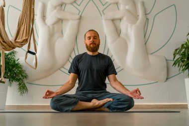 Sakallı yetişkin bir adam, parlak bir yoga stüdyosunda gözleri kapalı meditasyon yapar.