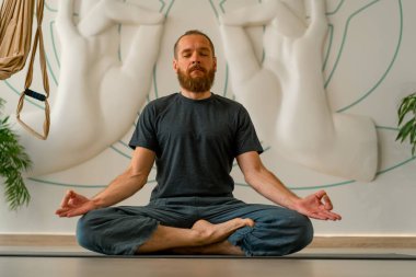 Sakallı yetişkin bir adam, parlak bir yoga stüdyosunda gözleri kapalı meditasyon yapar.