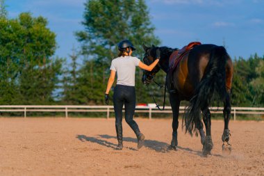 Miğferli bir sürücü, güzel siyah atına biniş pistindeki koşum takımının yanında liderlik eder.