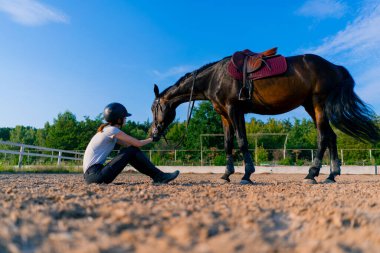 Bir miğferli binici, at binerken güzel siyah atını elinden besliyor.