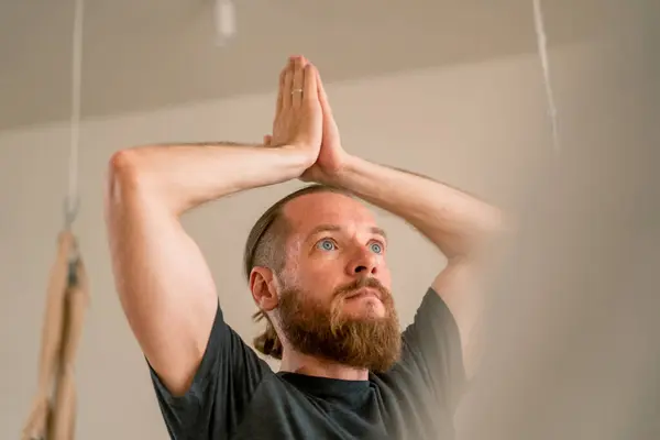 close-up of a man with a beard in a yoga room who  doing yoga his hands are raised up his face is focused