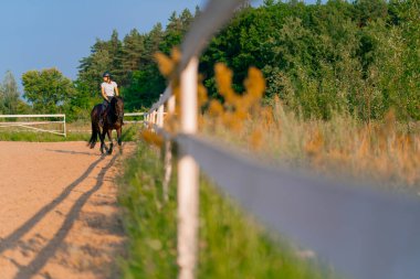 Miğfer takmış bir atlı kadın ata binerken arenada güzel siyah atına biniyor.