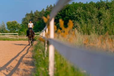 Miğfer takmış bir atlı kadın ata binerken arenada güzel siyah atına biniyor.