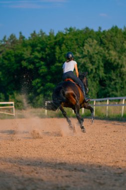 Miğfer takmış bir atlı kadın ata binerken arenada güzel siyah atına biniyor.