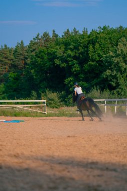 Miğfer takmış bir atlı kadın ata binerken arenada güzel siyah atına biniyor.