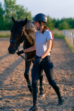 Miğferli bir sürücü, güzel siyah atına biniş pistindeki koşum takımının yanında liderlik eder.
