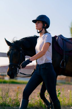 Miğferli bir sürücü, güzel siyah atına biniş pistindeki koşum takımının yanında liderlik eder.