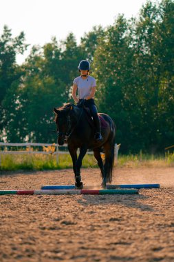 Miğfer takmış bir binici ata binerken güzel siyah atını bir arenada sürüyor.