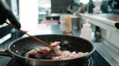 Bir restoranda profesyonel bir mutfakta şef tavada sulu tavuk filetosu pişiriyor.
