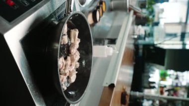 Bir restoranda, profesyonel bir mutfakta şefin tavaya yakın dikey bir videoda sulu tavuk filetosu pişirmesi.