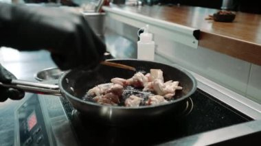 Bir restoranda profesyonel bir mutfakta şef tavada sulu tavuk filetosu pişiriyor.