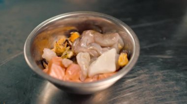 Siyah eldivenli bir şefin yakın plan çekimi. Pişirmeden önce içinde deniz mahsulleri olan tabaktan streç film çıkarıyor.