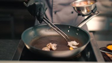 Otelin restoranındaki profesyonel mutfak. Şef, tavada maşayla deniz mahsulleri hazırlıyor. Asya mutfağı yakın plan.