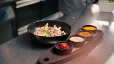 Profesyonel bir mutfakta, deniz ürünleri sotesi hazırlayan bir şefin yakın plan çekimi. Bebek ahtapotla maşayı bir tavada karıştırıyor.