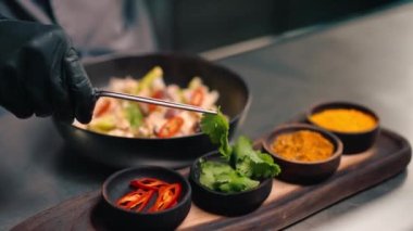 Profesyonel mutfakta, deniz ürünleri sotelenmiş maşayla yeşillik ekleyen şefin yakın çekimi.