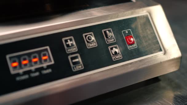プロのキッチンの誘導ストーブをオンにするためにボタンを押すシェフの指のクローズアップ — ストック動画