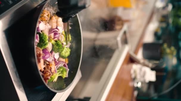 一名厨师在专业厨房里的特写镜头 准备用平底锅将海鲜调味配料倒入空气中的垂直视频 — 图库视频影像