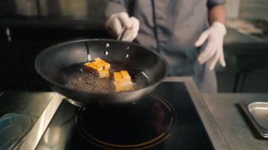 Profesyonel restoran aşçısı tavada tofu peyniri kızartıyor ve Asya mutfağına döküyor.