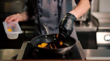 Yakın plan aşçı tavada baharatlı şeftali ve patates kızartması pişirir.
