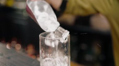 Bir barmenin yakın çekimi lezzetli kokteyller hazırlamak için bir kokteyl bardağına buz doldurur.