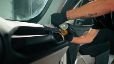 Detaylı işlemler sırasında araba yıkama işçisinin fırça ve araba kimyasalları kullanarak lüks bir arabanın gösterge tablosunu temizlemesi.