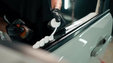 Detaylı işlemler sırasında lüks bir arabanın kapı kartını temizlerken plastik fırça kullanan bir oto yıkama işçisinin yakın çekimi.
