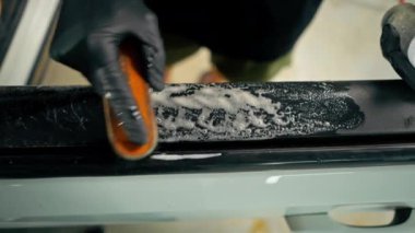 Detaylı işlemler sırasında lüks bir arabanın kapı kartını temizlerken plastik fırça kullanan bir oto yıkama işçisinin yakın çekimi.