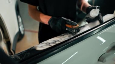 Detaylı işlemler sırasında lüks bir arabanın kapı kartını temizlerken plastik fırça kullanan bir oto yıkama işçisinin yakın çekimi.