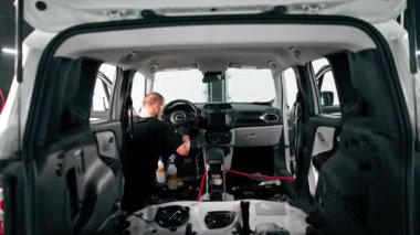 Detaylı işlemler sırasında araba yıkama işçisinin fırça ve araba kimyasalları kullanarak lüks bir arabanın gösterge tablosunu temizlemesi.