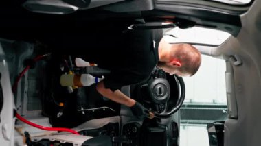 Lüks bir arabanın ön panelini temizlemek için fırça ve araba kimyasalları kullanan bir oto yıkama işçisinin yakın çekimi.