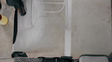 Temizleme işlemi sırasında elektrikli süpürge kullanarak beyaz araba koltuklarını temizleyen bir oto yıkama işçisi.